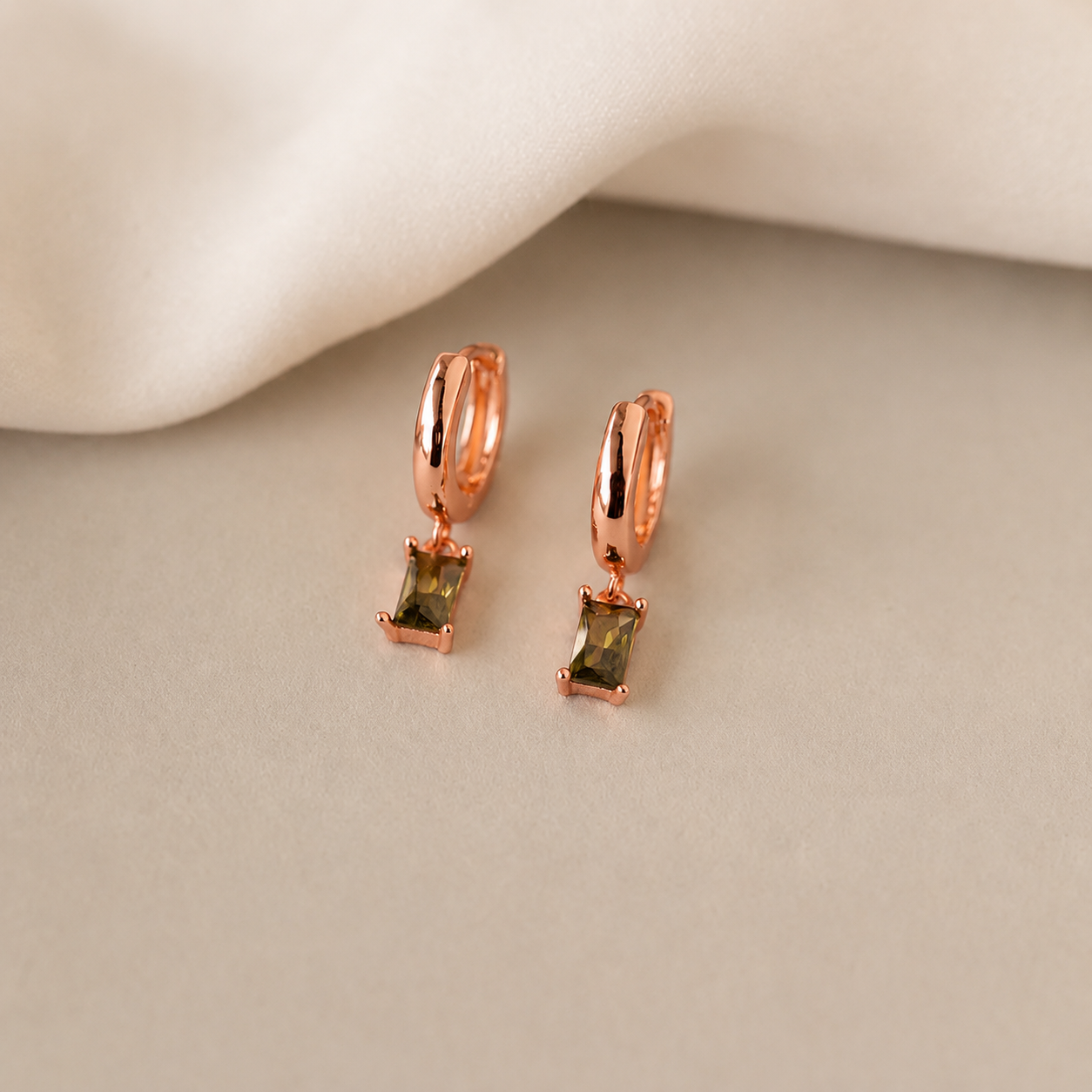 Rose gold hoop earrings with green gemstones on a beige surface